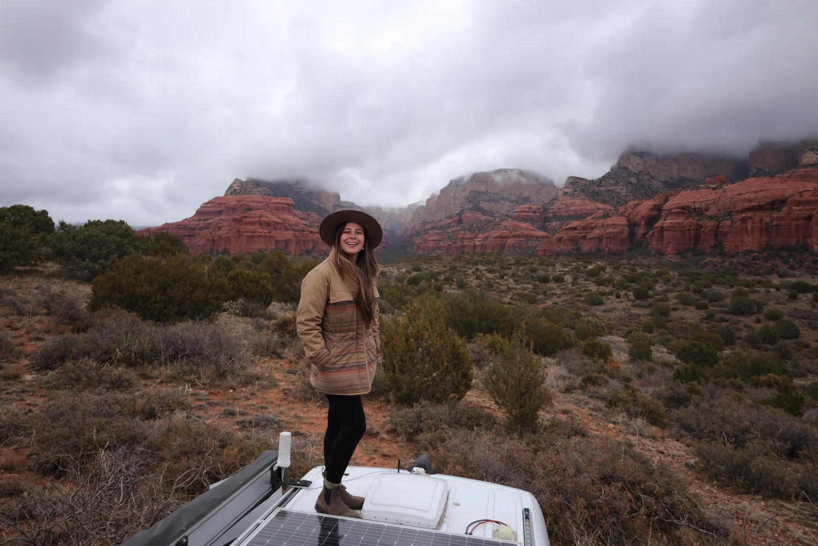 Mariajosé standing on a campervan beneath desert cliffs.